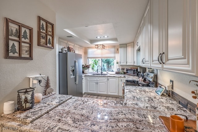 kitchen featuring light stone counters, stainless steel appliances, a raised ceiling, sink, and white cabinets