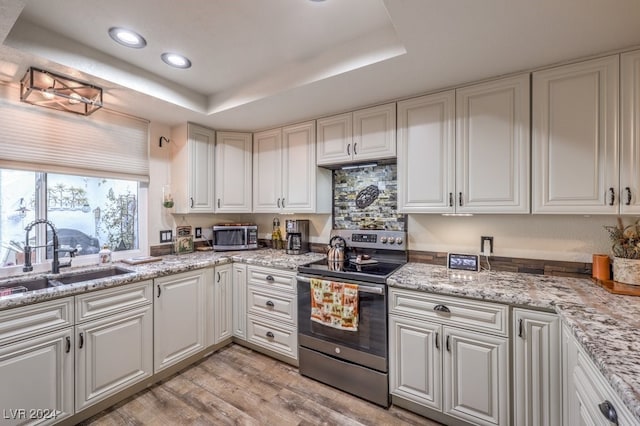 kitchen featuring white cabinetry, sink, light hardwood / wood-style flooring, a tray ceiling, and stainless steel range with electric cooktop