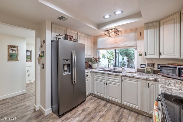 kitchen with appliances with stainless steel finishes, a tray ceiling, white cabinetry, and sink