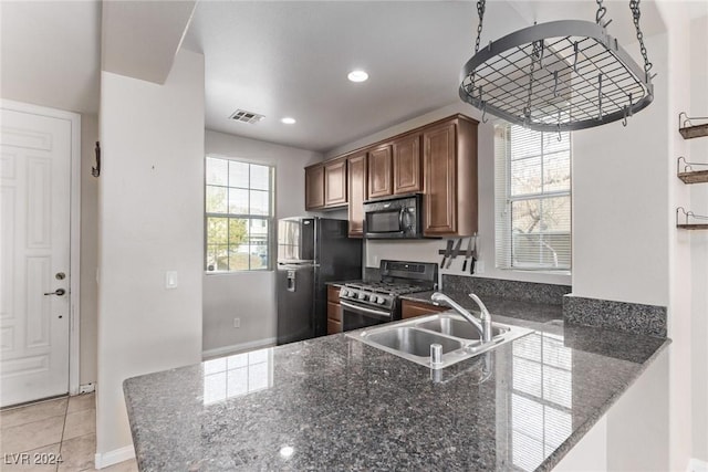 kitchen with sink, kitchen peninsula, dark stone counters, light tile patterned floors, and black appliances