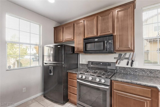 kitchen with black appliances, plenty of natural light, dark stone countertops, and light tile patterned floors