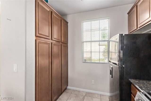 kitchen featuring dark stone countertops, light tile patterned floors, and fridge