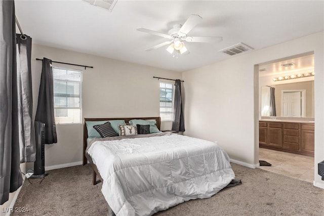 bedroom with ceiling fan, light colored carpet, and ensuite bath