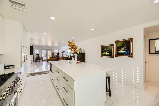 kitchen with white cabinets, a center island, french doors, a kitchen breakfast bar, and stainless steel stove