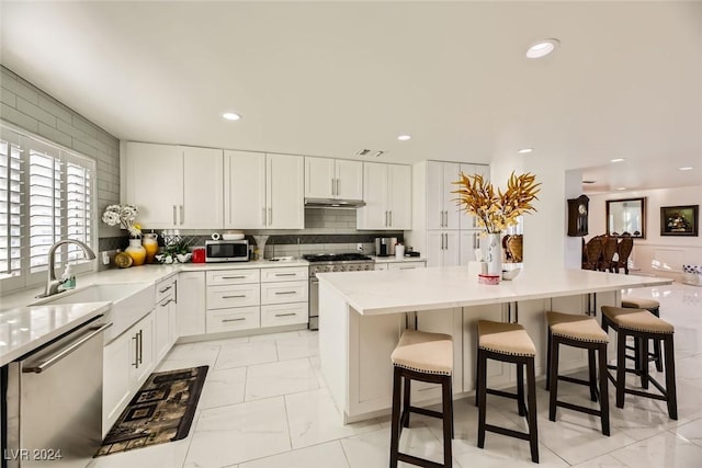 kitchen with white cabinets, appliances with stainless steel finishes, a center island, sink, and a breakfast bar area