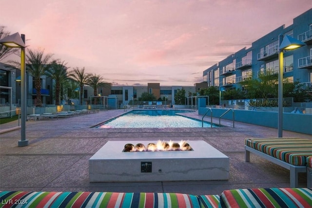 pool at dusk with an outdoor fire pit, fence, and a patio