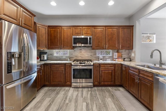 kitchen with sink, backsplash, stainless steel appliances, light stone counters, and light wood-type flooring