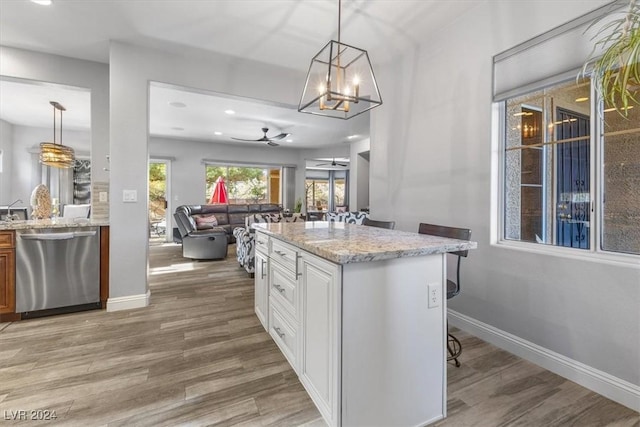 kitchen with pendant lighting, dishwasher, white cabinetry, light stone counters, and a kitchen bar