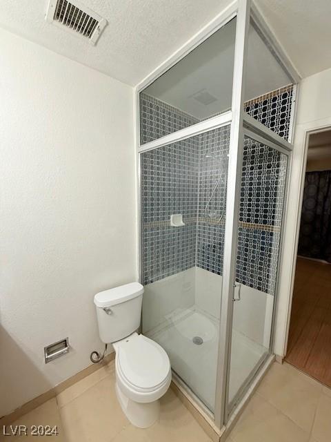 full bathroom featuring visible vents, toilet, a textured ceiling, a shower stall, and tile patterned floors