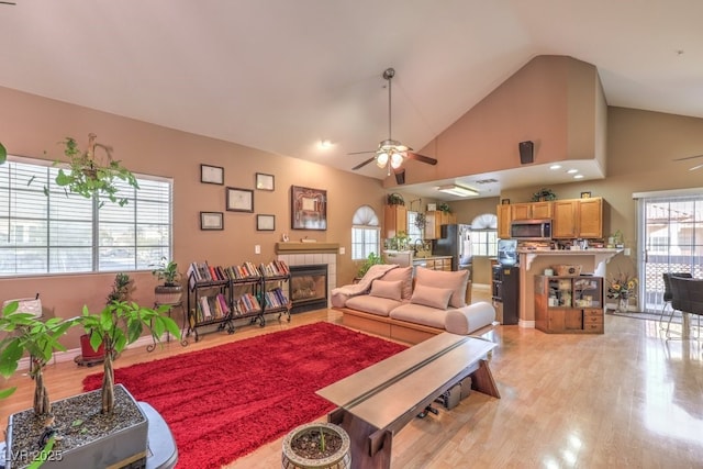 living room featuring light hardwood / wood-style floors, ceiling fan, a tile fireplace, and high vaulted ceiling