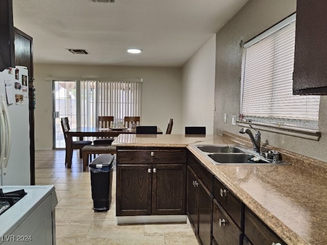 kitchen featuring kitchen peninsula, sink, white fridge, and dark brown cabinets