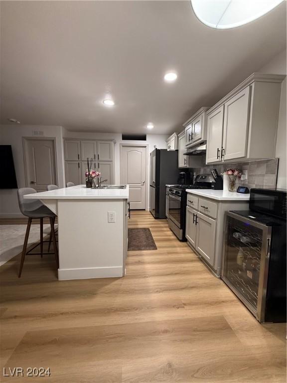 kitchen with black appliances, light hardwood / wood-style flooring, decorative backsplash, a kitchen island, and a kitchen bar