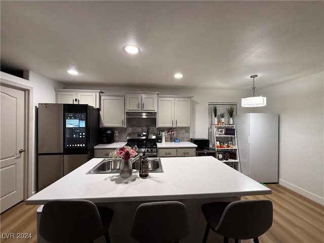 kitchen with tasteful backsplash, a kitchen breakfast bar, light hardwood / wood-style floors, a kitchen island with sink, and appliances with stainless steel finishes