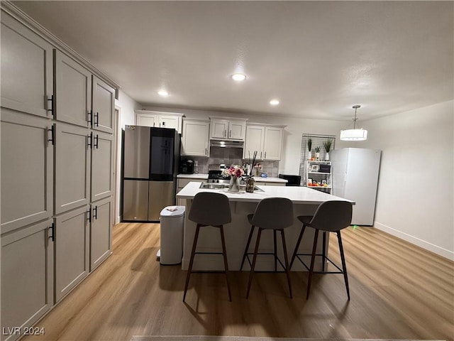 kitchen with appliances with stainless steel finishes, a kitchen breakfast bar, tasteful backsplash, light hardwood / wood-style flooring, and hanging light fixtures