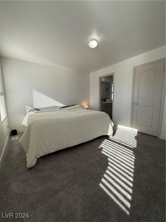 bedroom with connected bathroom and dark carpet