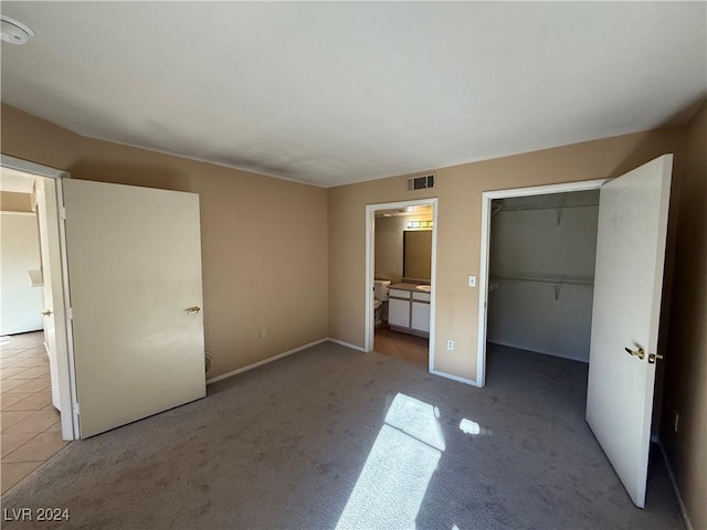 unfurnished bedroom with ensuite bathroom, a closet, and light colored carpet