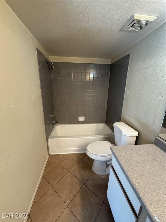 full bathroom with tile patterned floors, a textured ceiling, vanity, tiled shower / bath combo, and toilet