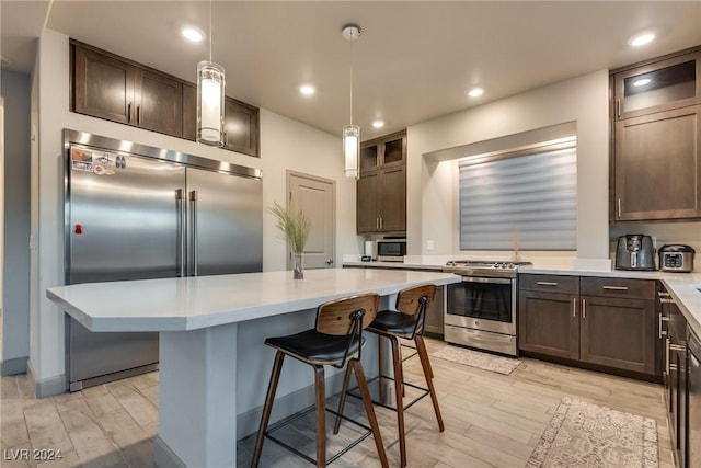 kitchen with dark brown cabinetry, stainless steel appliances, light hardwood / wood-style floors, a kitchen island, and hanging light fixtures