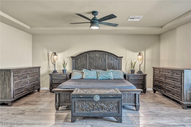 bedroom featuring light hardwood / wood-style floors, ceiling fan, and a tray ceiling