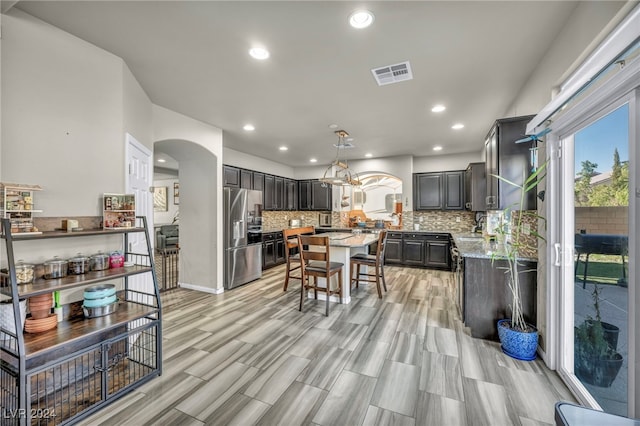 kitchen with a notable chandelier, stainless steel fridge, light stone counters, decorative backsplash, and sink