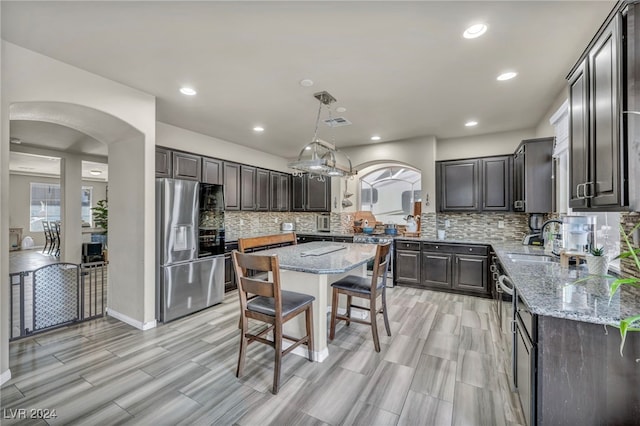 kitchen featuring stainless steel appliances, hanging light fixtures, a center island, light stone countertops, and backsplash