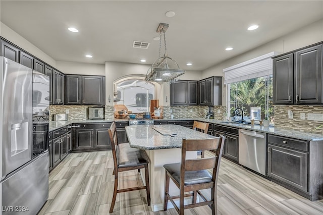 kitchen with sink, light stone countertops, a kitchen island, pendant lighting, and appliances with stainless steel finishes