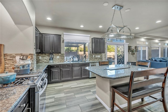 kitchen with light stone counters, decorative backsplash, a kitchen island, pendant lighting, and appliances with stainless steel finishes