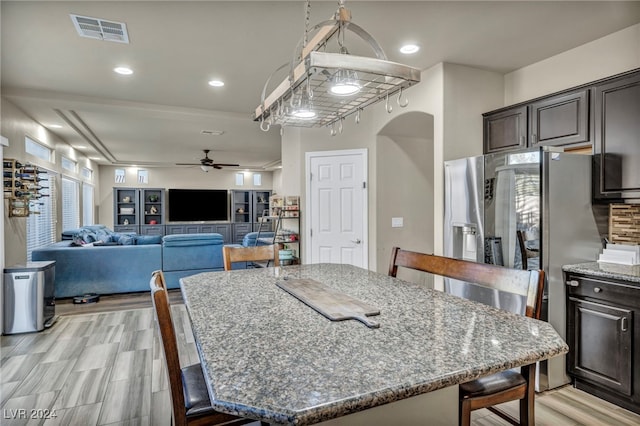 kitchen with a kitchen island, ceiling fan, stone counters, and dark brown cabinetry