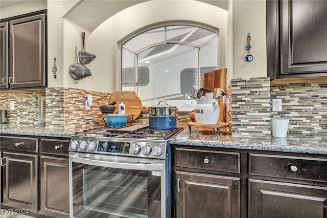 kitchen with stainless steel range, stone countertops, dark brown cabinets, and decorative backsplash