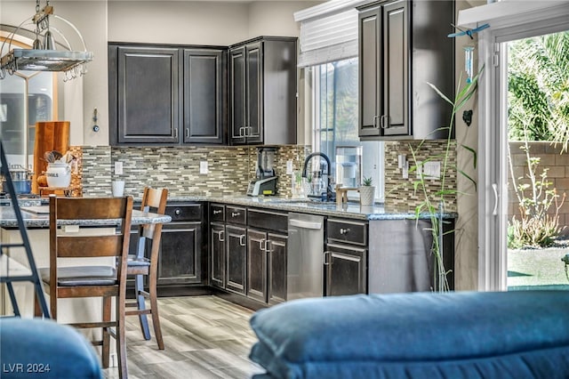 kitchen featuring dishwasher, light hardwood / wood-style floors, light stone countertops, sink, and backsplash