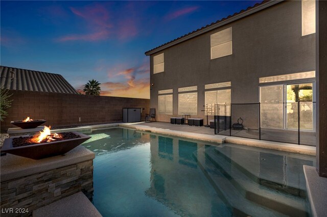 pool at dusk featuring a fire pit and a patio