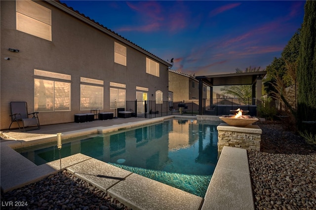 pool at dusk with a fire pit and a patio area