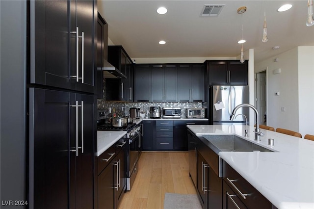 kitchen with stainless steel appliances, backsplash, pendant lighting, exhaust hood, and light wood-type flooring