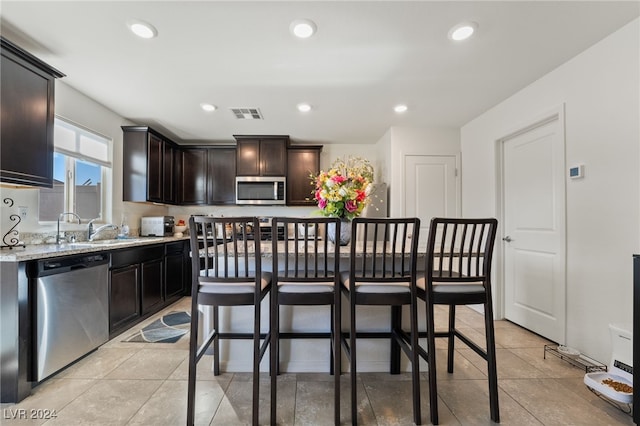 kitchen featuring a kitchen bar, light stone counters, dark brown cabinets, a kitchen island, and stainless steel appliances