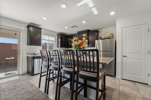 kitchen featuring dark brown cabinetry, light tile patterned floors, light stone counters, and appliances with stainless steel finishes