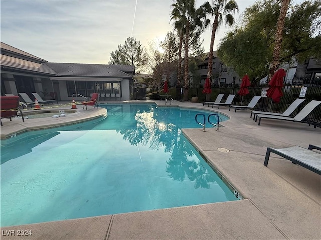 pool at dusk featuring a patio area and a community hot tub