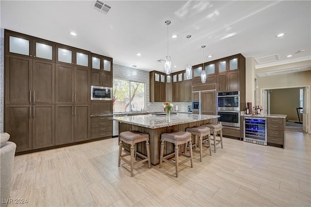 kitchen with a kitchen island, decorative light fixtures, wine cooler, built in appliances, and light stone countertops