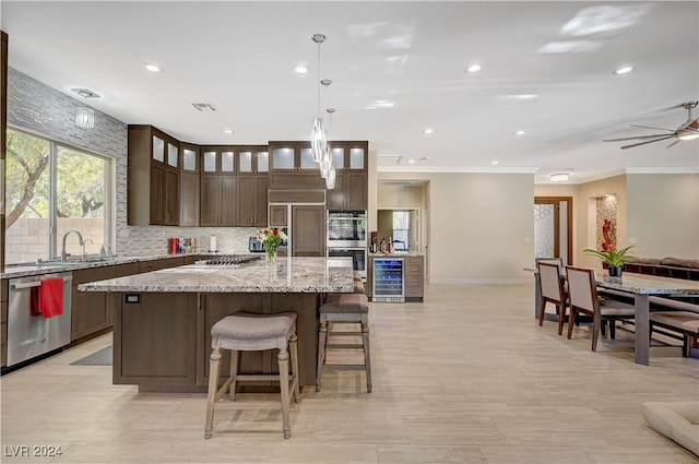 kitchen featuring appliances with stainless steel finishes, a center island, light stone countertops, decorative light fixtures, and beverage cooler