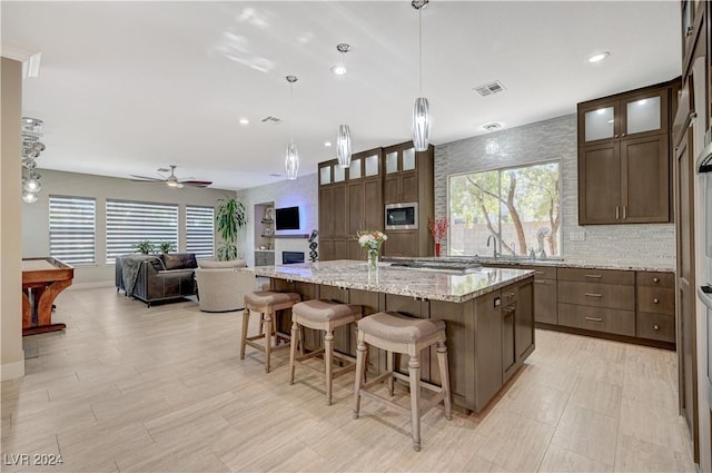 kitchen featuring ceiling fan, a center island, stainless steel microwave, light stone countertops, and decorative light fixtures