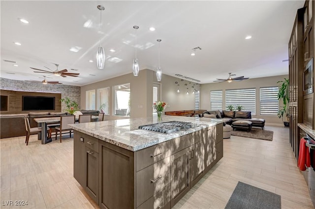 kitchen featuring appliances with stainless steel finishes, decorative light fixtures, a large island, ceiling fan, and light stone counters