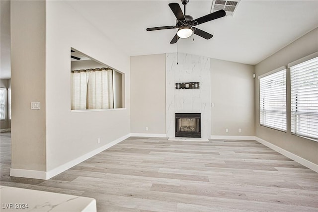 unfurnished living room with ceiling fan, a premium fireplace, vaulted ceiling, and light wood-type flooring