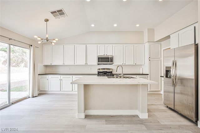 kitchen with appliances with stainless steel finishes, vaulted ceiling, a kitchen island with sink, sink, and decorative light fixtures