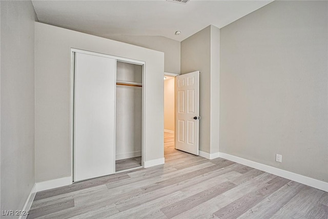 unfurnished bedroom with light wood-type flooring, lofted ceiling, and a closet