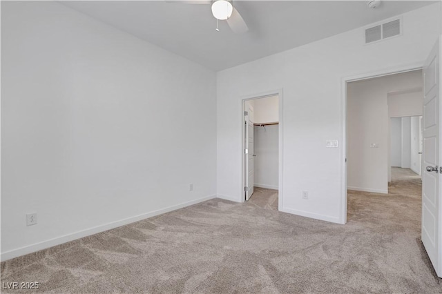 unfurnished bedroom featuring light colored carpet, a closet, ceiling fan, and a spacious closet