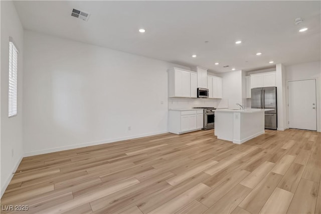 kitchen with a center island with sink, high quality appliances, white cabinets, light hardwood / wood-style flooring, and backsplash