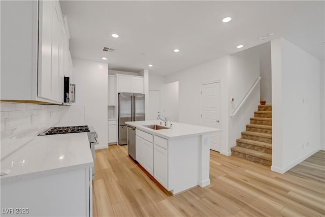 kitchen featuring sink, white cabinets, light wood-type flooring, a kitchen island with sink, and appliances with stainless steel finishes