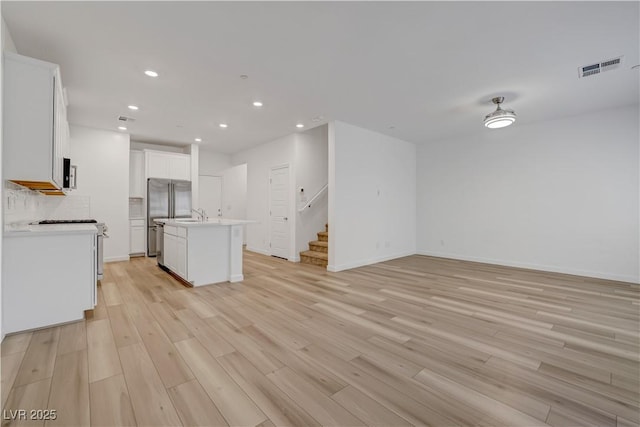 kitchen with sink, white cabinetry, light wood-type flooring, and a center island with sink