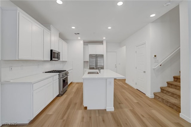 kitchen with white cabinetry, light wood-type flooring, a center island with sink, and premium appliances