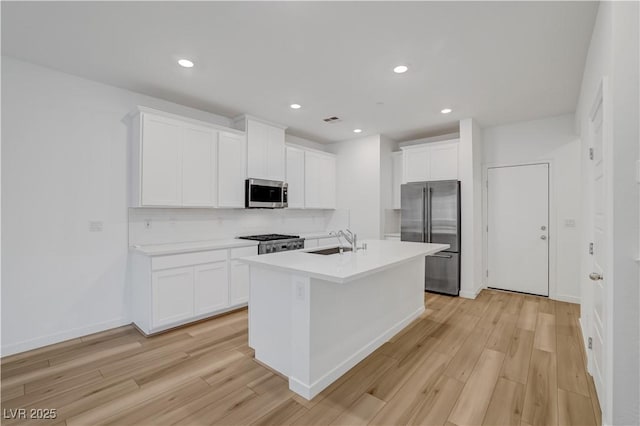 kitchen featuring an island with sink, light hardwood / wood-style floors, decorative backsplash, white cabinets, and appliances with stainless steel finishes