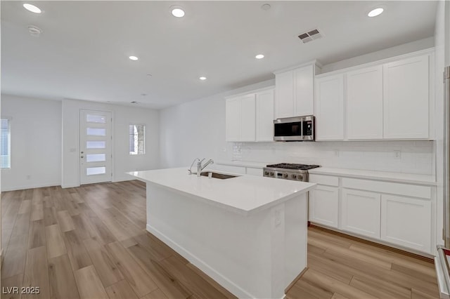 kitchen featuring white cabinets, light hardwood / wood-style flooring, decorative backsplash, range, and a kitchen island with sink